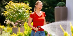 Frau mit Gartenschlauch bewässert Pflanzen